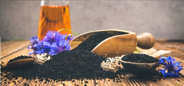 Nigella oil seeds and flower on wooden table with space